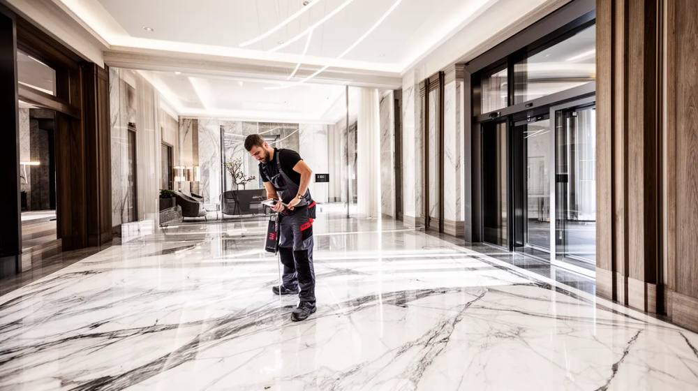 Homme en uniforme nettoyant un sol de marbre dans un hall d'entrée élégant.