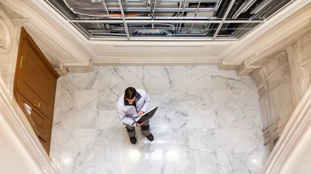 Homme en costume travaillant sur ordinateur portable dans un hall d'entrée en marbre.
