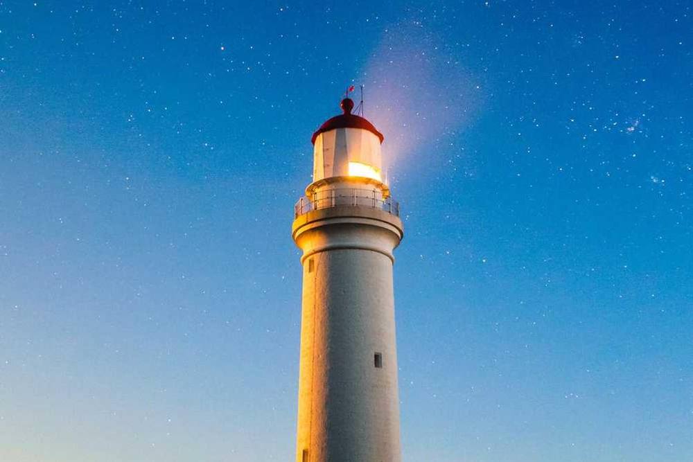 Le faisceau du phare brille contre un ciel étoilé.