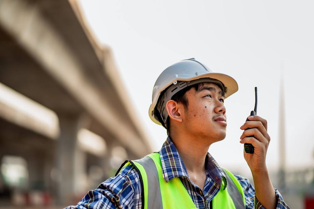 Jeune ouvrier de chantier portant un casque de sécurité et utilisant une radio.
