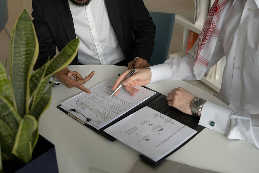 Deux hommes assis à une table avec des documents et un stylo.