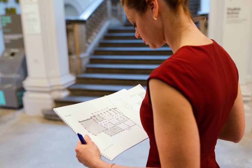 Femme en robe rouge examinant attentivement un plan architectural.