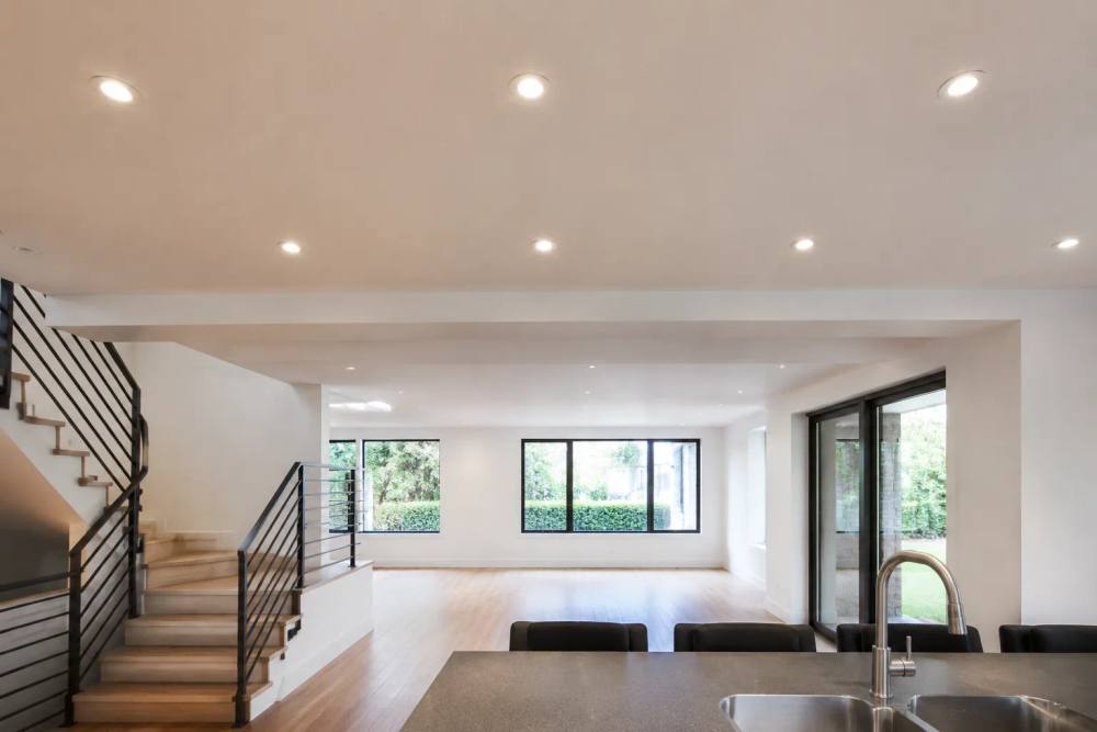 Intérieur lumineux et moderne avec escalier, fenêtres panoramiques et cuisine ouverte.