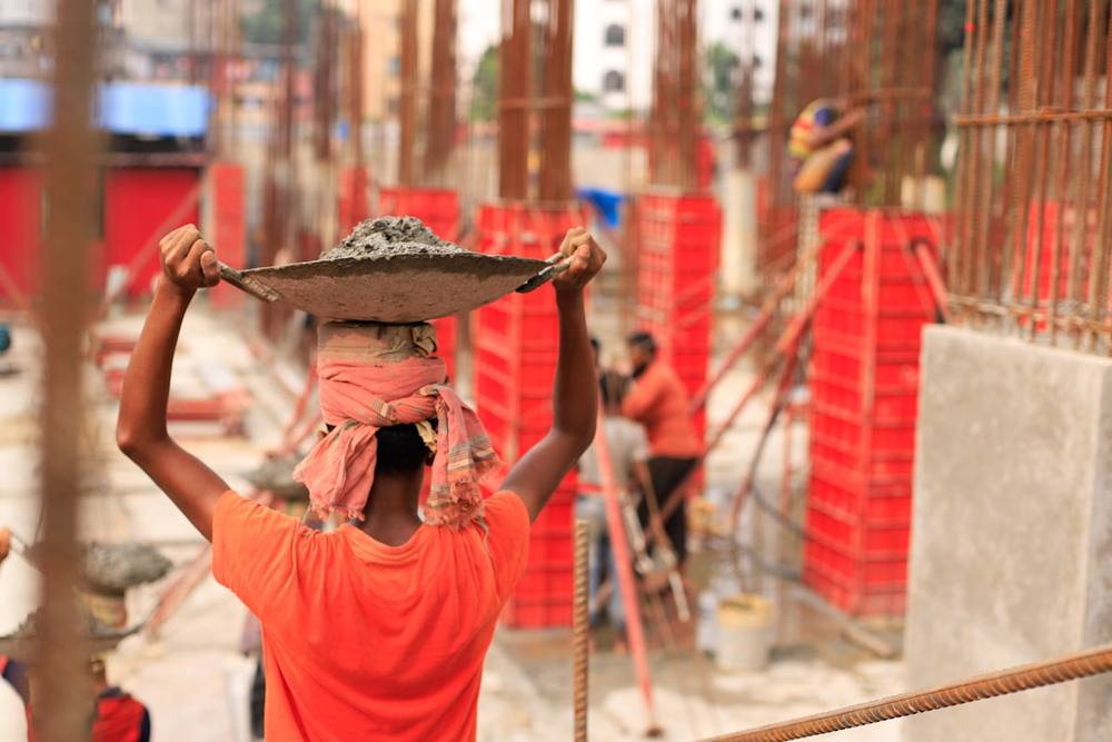 Une femme en chemise orange portant un plateau sur la tête.