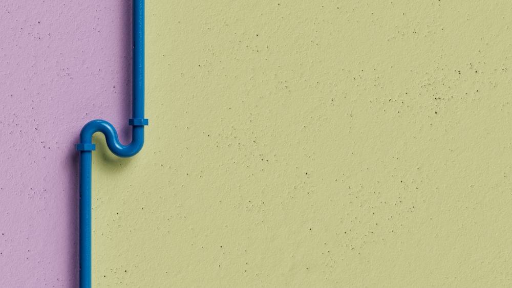 Un tuyau bleu sur un mur jaune et violet.
