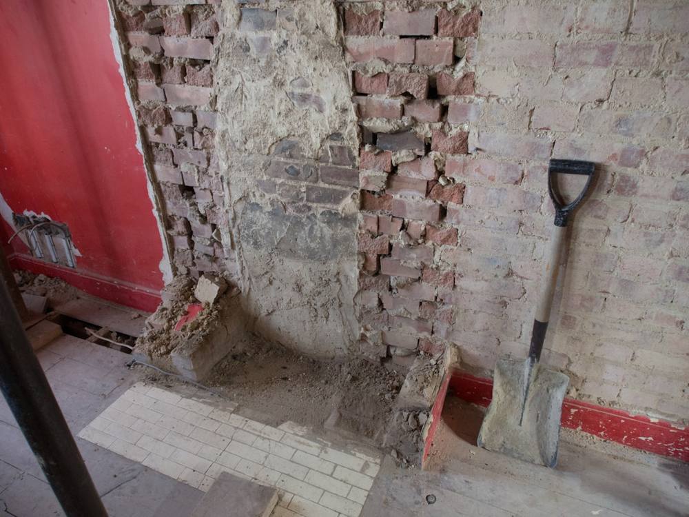 Une pelle noire appuyée contre un mur de briques brunes.
