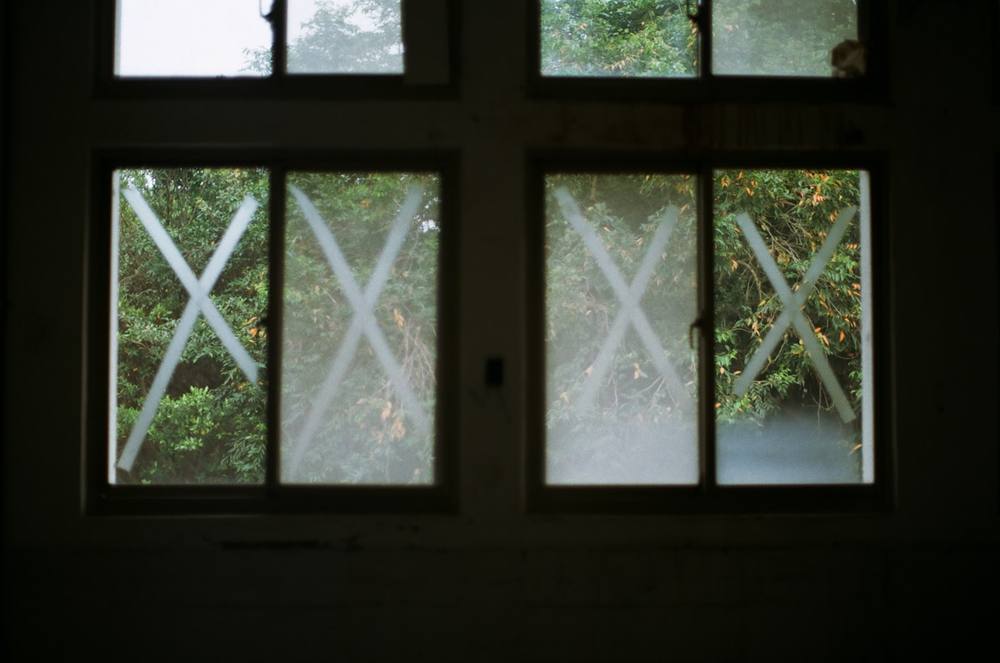 Fenêtre sombre avec motif en croix, vue sur la forêt verdoyante.
