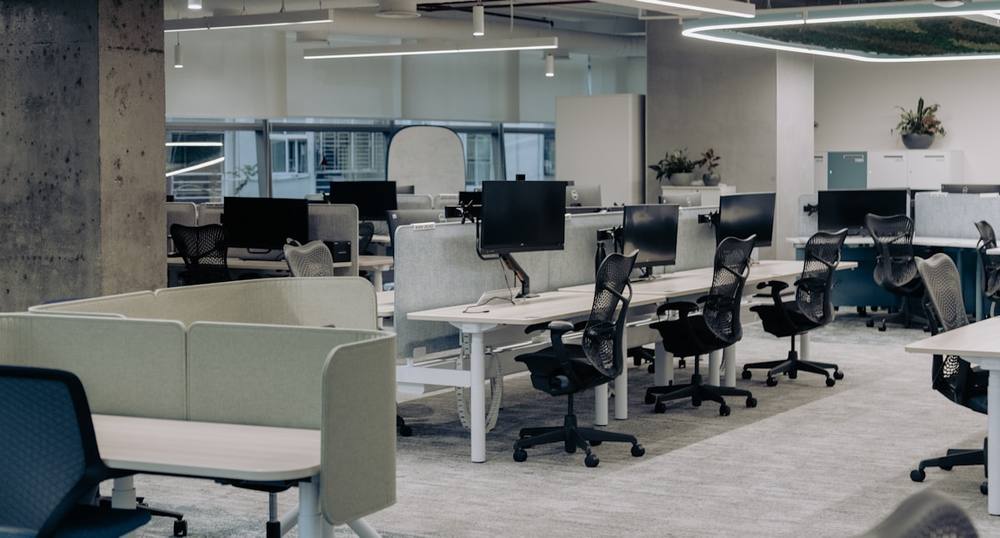 Espace de travail moderne avec bureaux, ordinateurs et plantes d'intérieur.