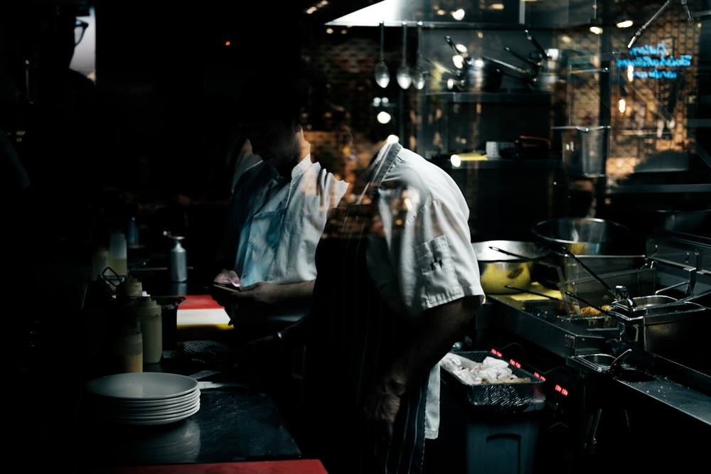 Deux chefs cuisinant dans une cuisine sombre et animée.