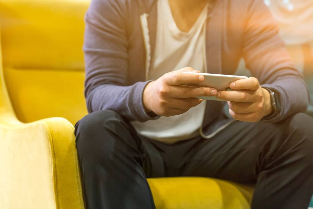 Une personne assise sur un canapé tenant un smartphone.