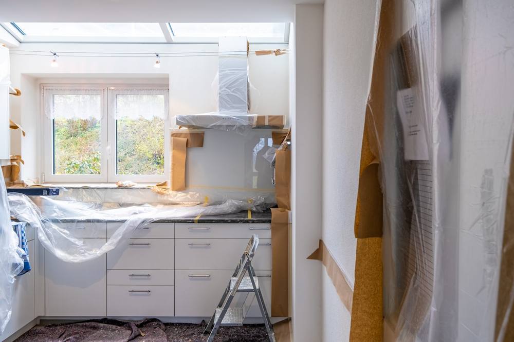 Cuisine en rénovation avec meubles emballés et échelle.