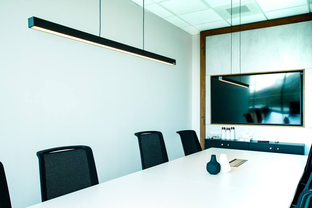 Salle de réunion moderne avec table blanche, chaises noires et écran mural.