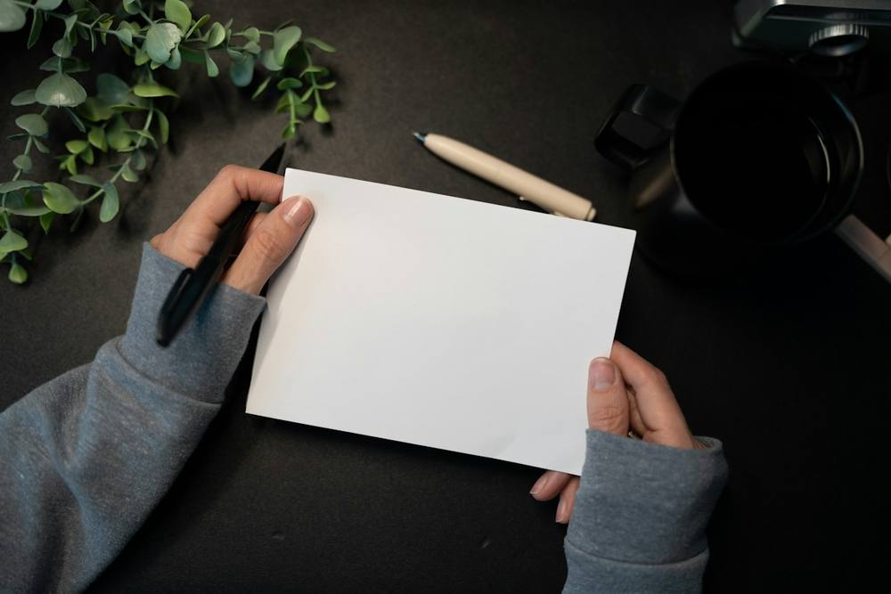 Mains tenant une feuille blanche au-dessus d’un bureau sombre.