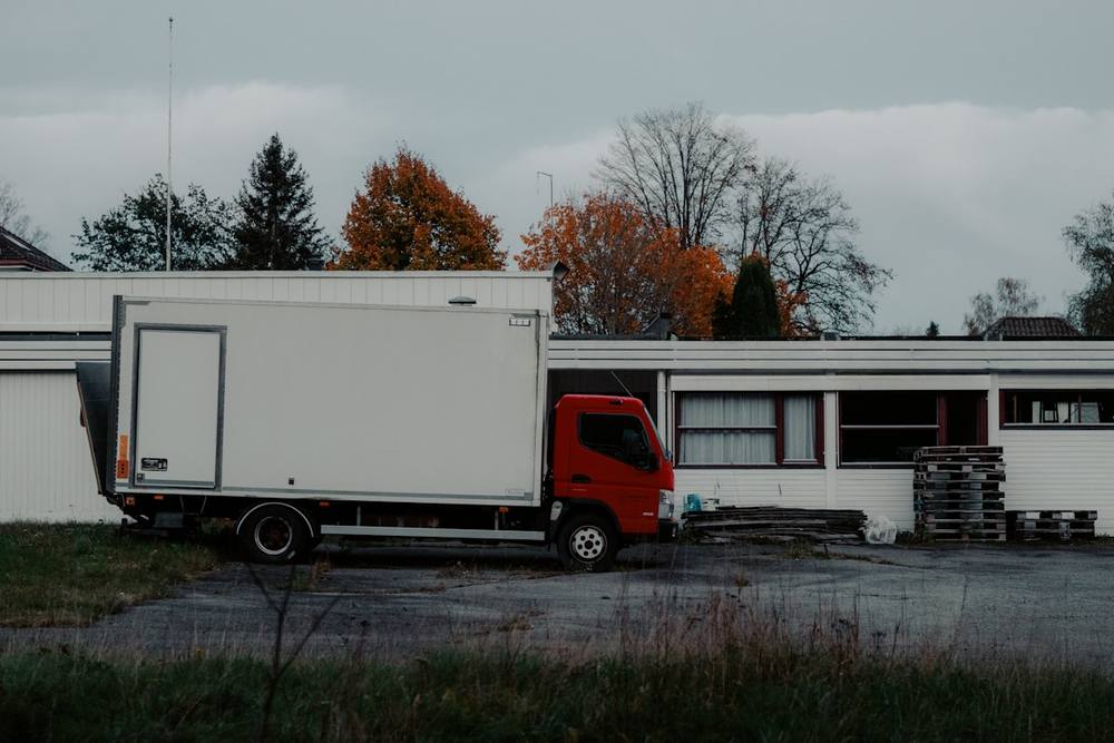 Camion de livraison rouge garé devant un bâtiment avec des arbres en automne.