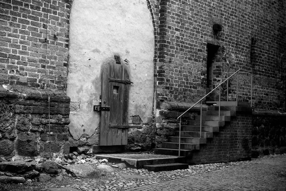 Porte en bois délabrée dans un mur de briques, escalier en pierre.