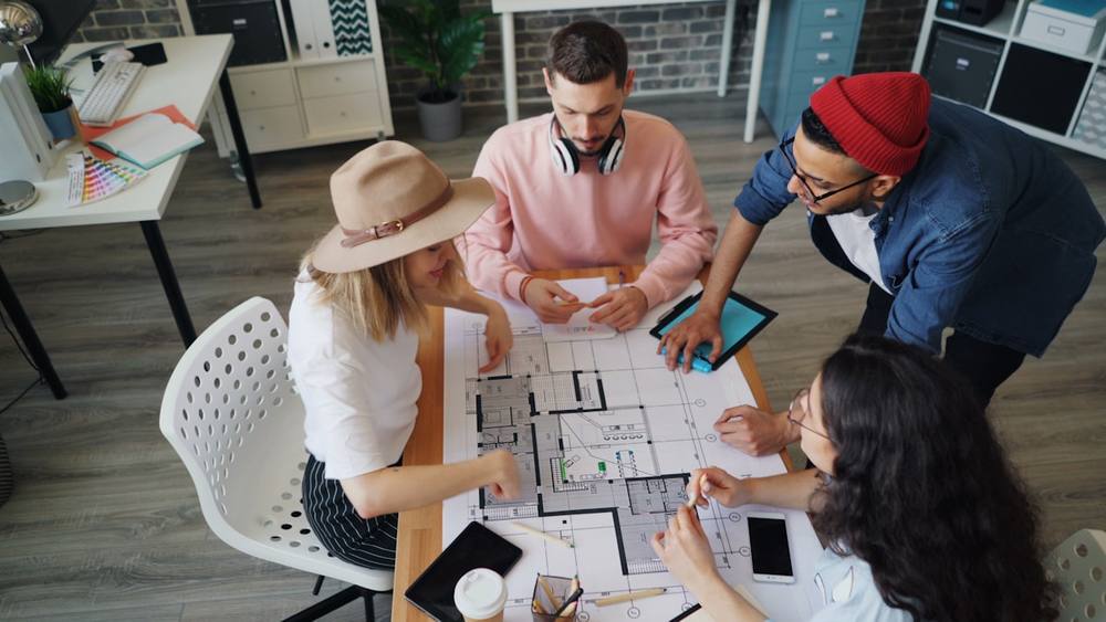 Groupe de concepteurs discutant d'un plan architectural sur une table.
