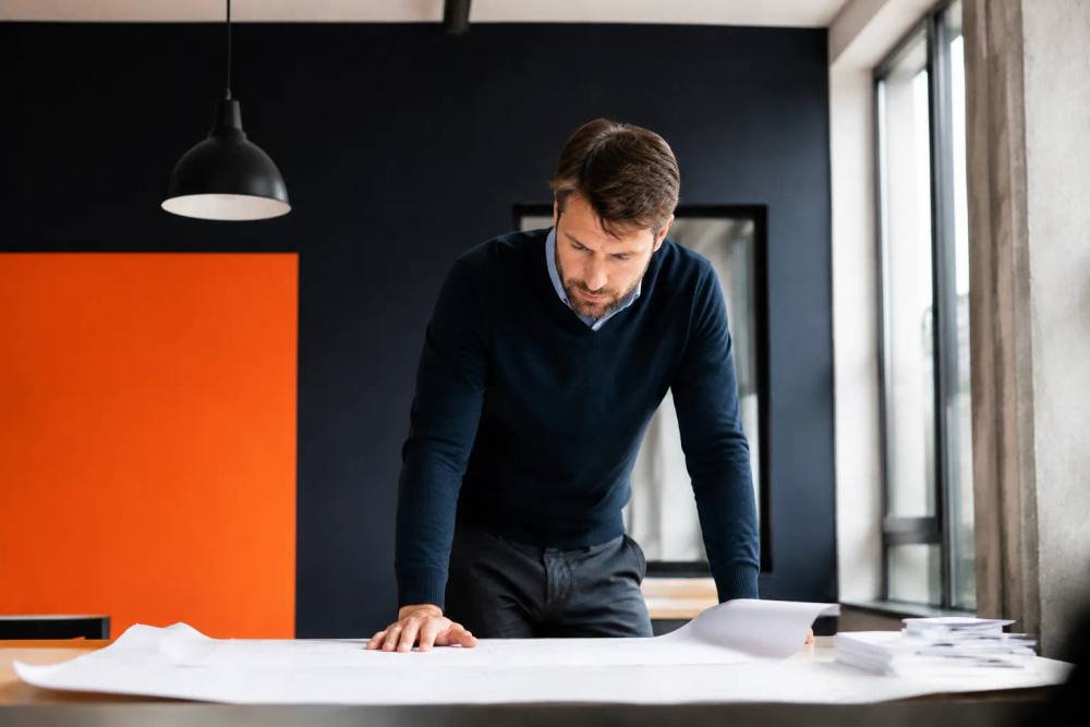 Homme d'affaires concentré examinant des plans sur un bureau.