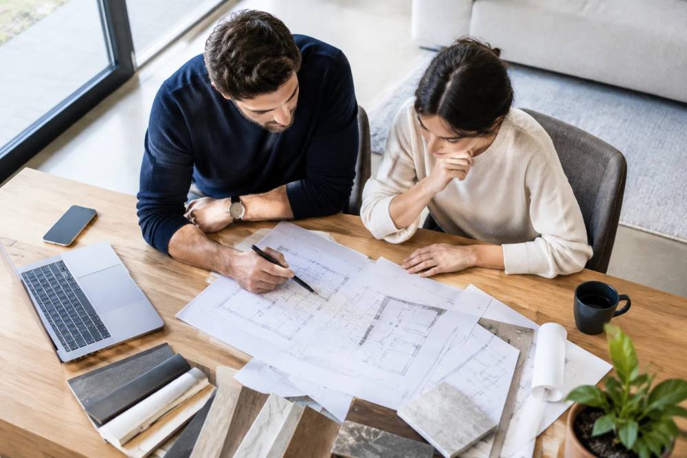 Deux personnes travaillant ensemble sur des plans architecturaux sur une table de bureau.