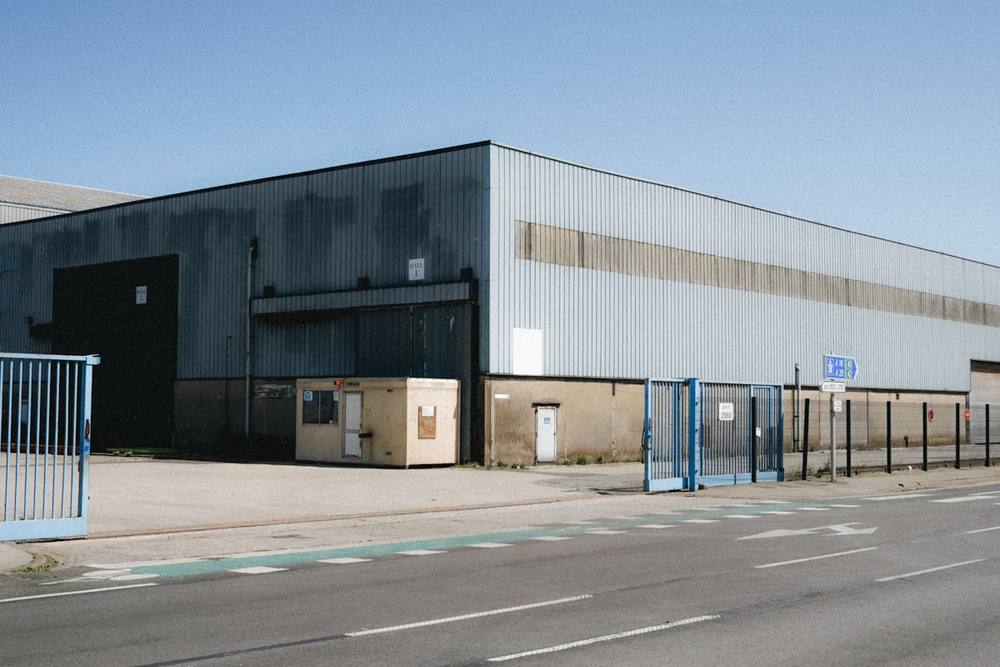 Vaste entrepôt industriel avec des portes bleues et une route.