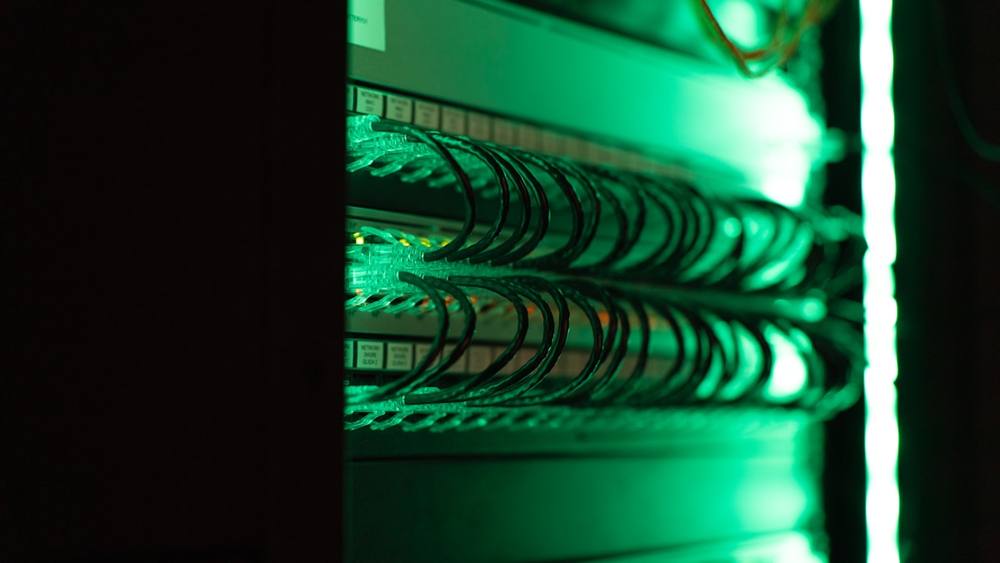Câbles réseau verts empilés dans un rack de serveur.