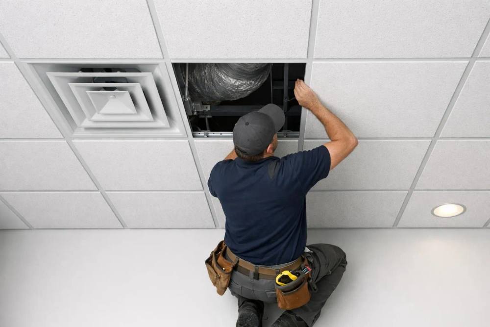 Un entrepreneur professionnel inspecte l'installation de panneaux de plafond acoustique dans un bureau commercial moderne, montrant un travail technique détaillé avec un système de grille de plafond suspendu et des points d'intégration de ventilation visibles, une lumière naturelle soulignant l'artisanat et la