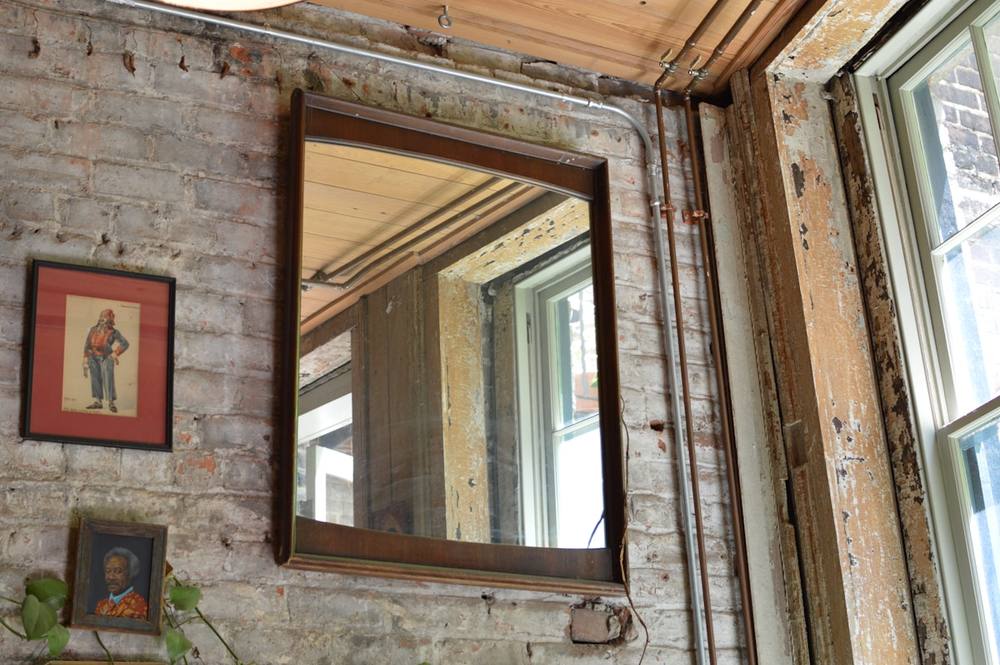 Miroir encadré sur mur de briques rustiques avec tuyaux apparents.