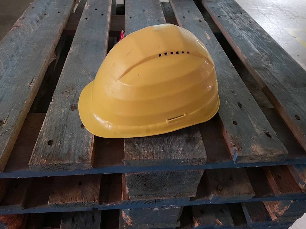 Un casque de sécurité jaune repose sur une palette en bois.