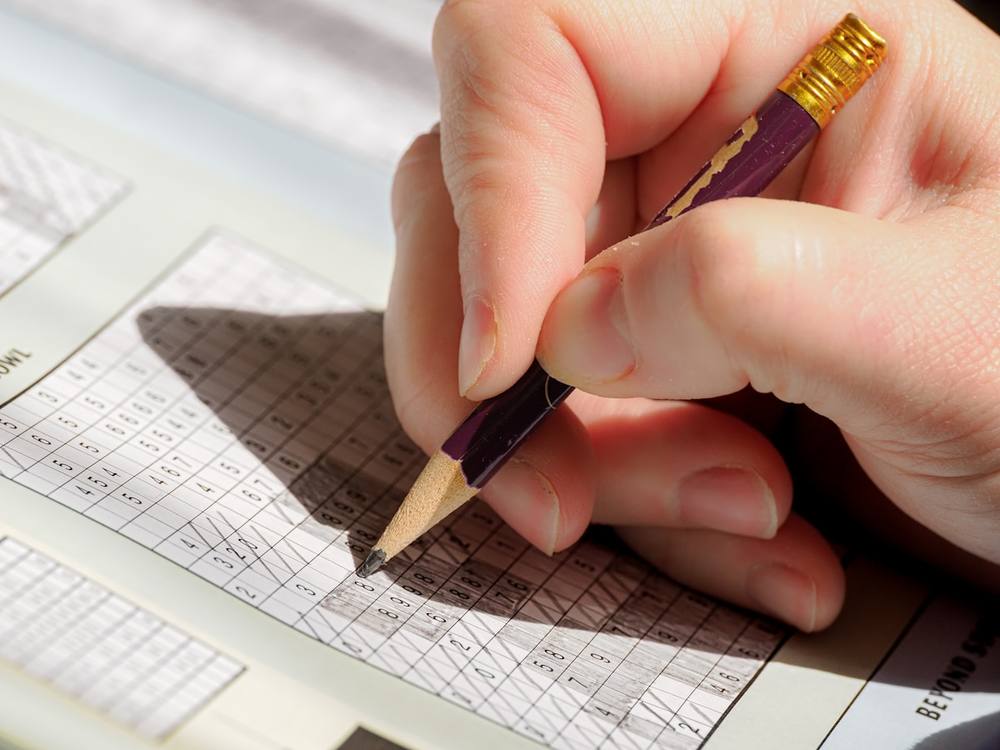 Une personne tenant un crayon et écrivant sur une feuille de papier.