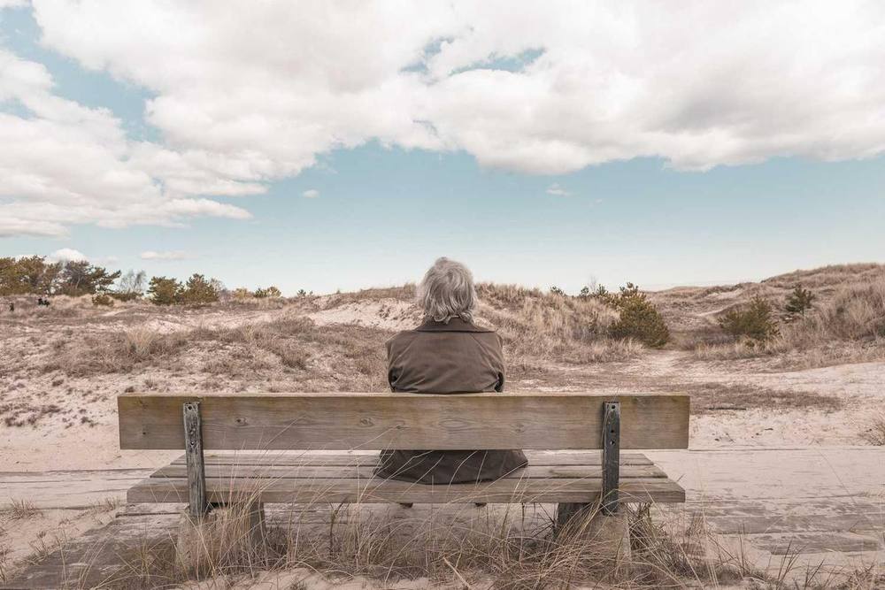 Une personne est assise sur un banc avec vue sur les dunes.